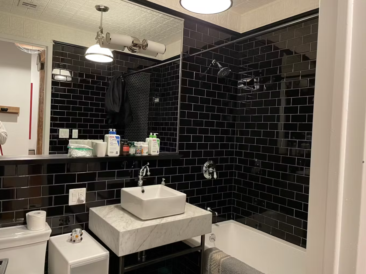 Bathroom in glossy black subway tile with a marble vanity and vessel sink