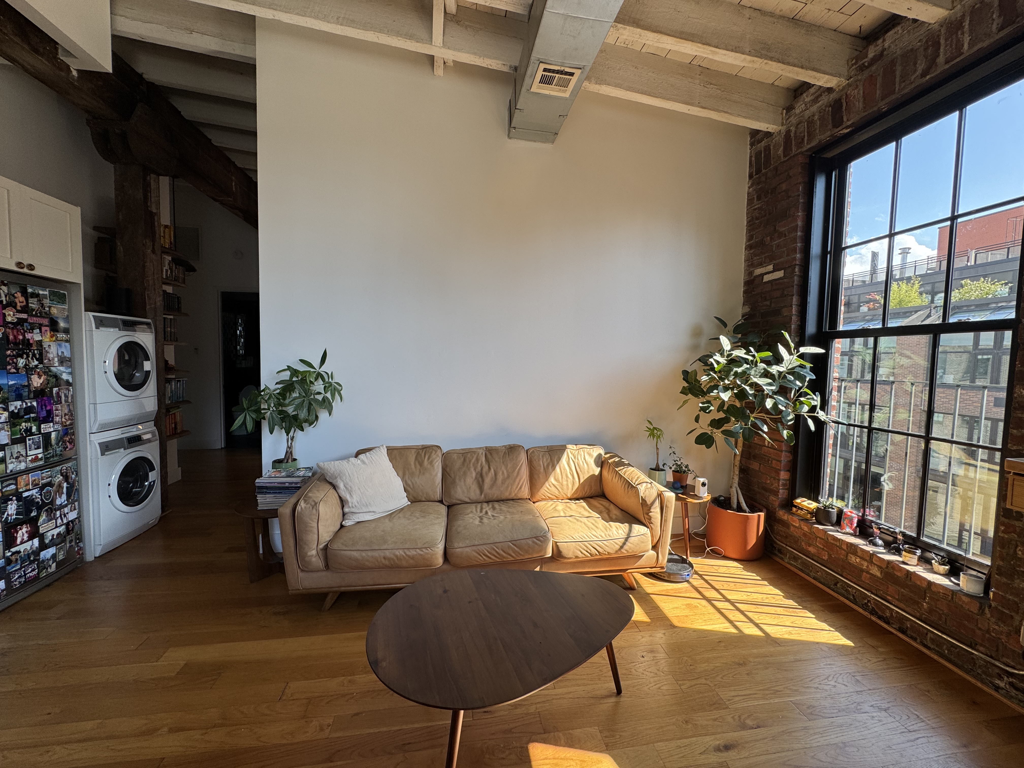 Tan leather sofa and walnut coffee table in warm afternoon light beside a tall paned factory window