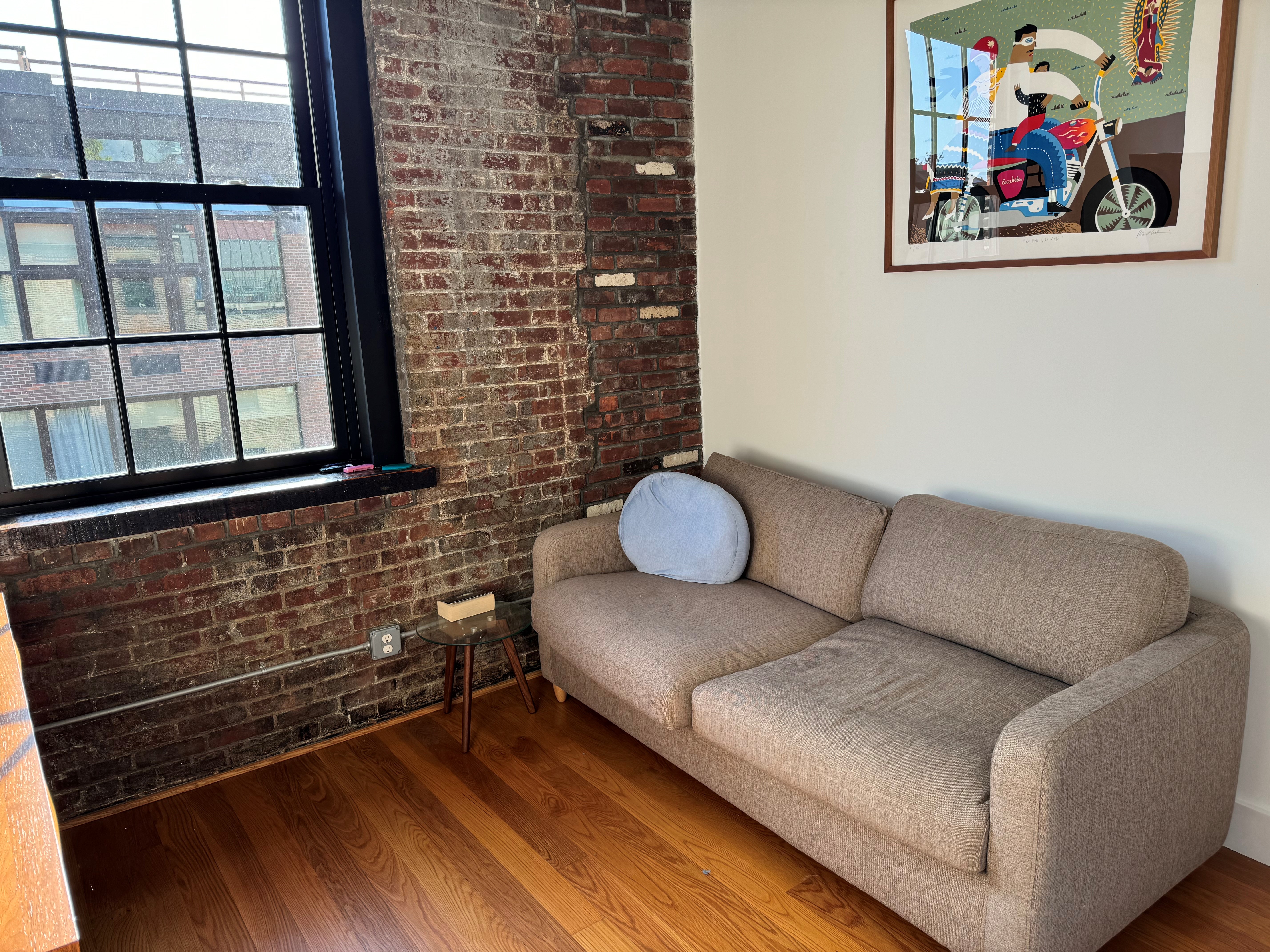 Second bedroom with a pull-out queen couch beside a large paned window and exposed brick