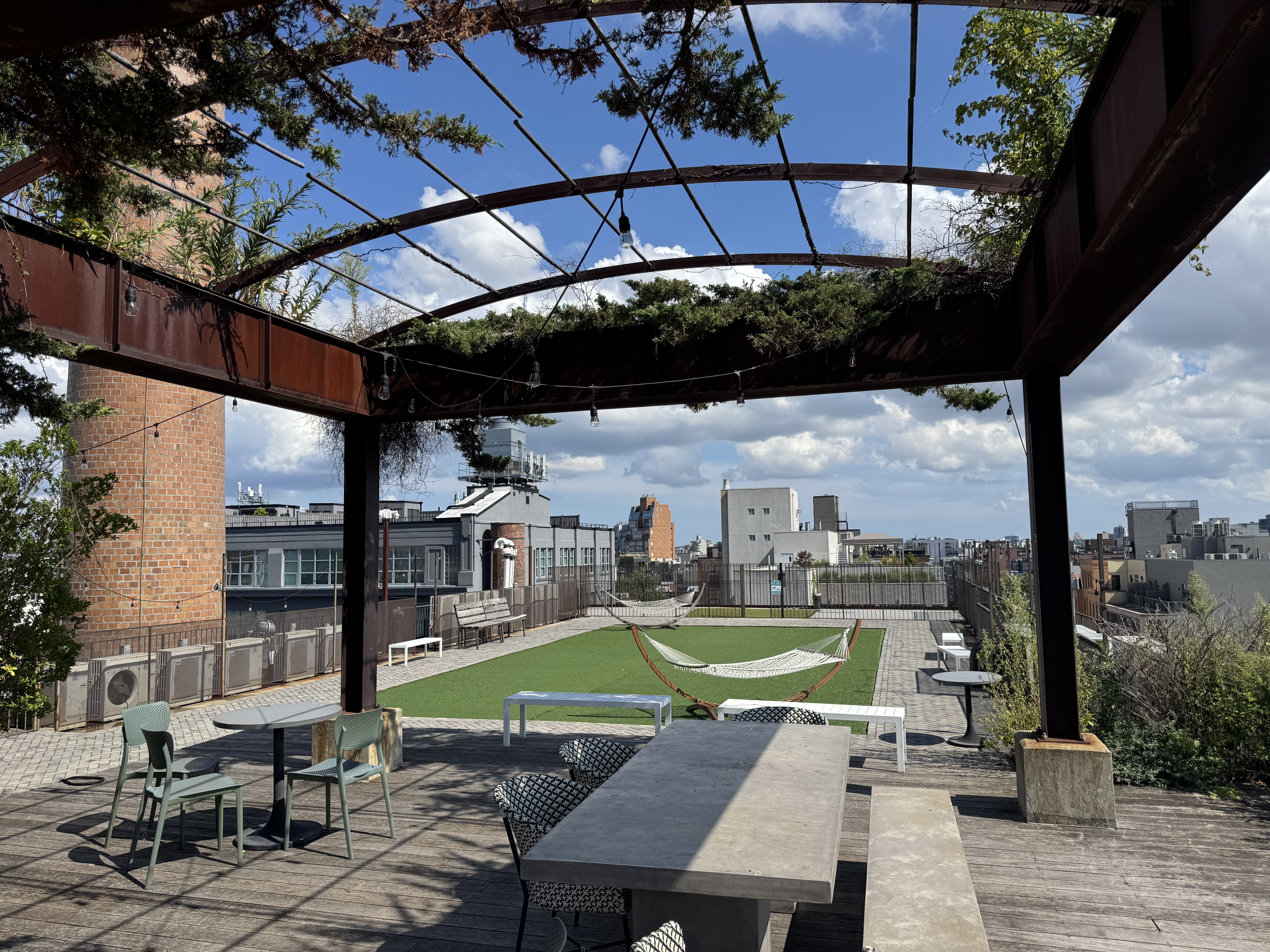 Shared roof deck with a vine-covered pergola, dining tables, and hammocks on a green lawn