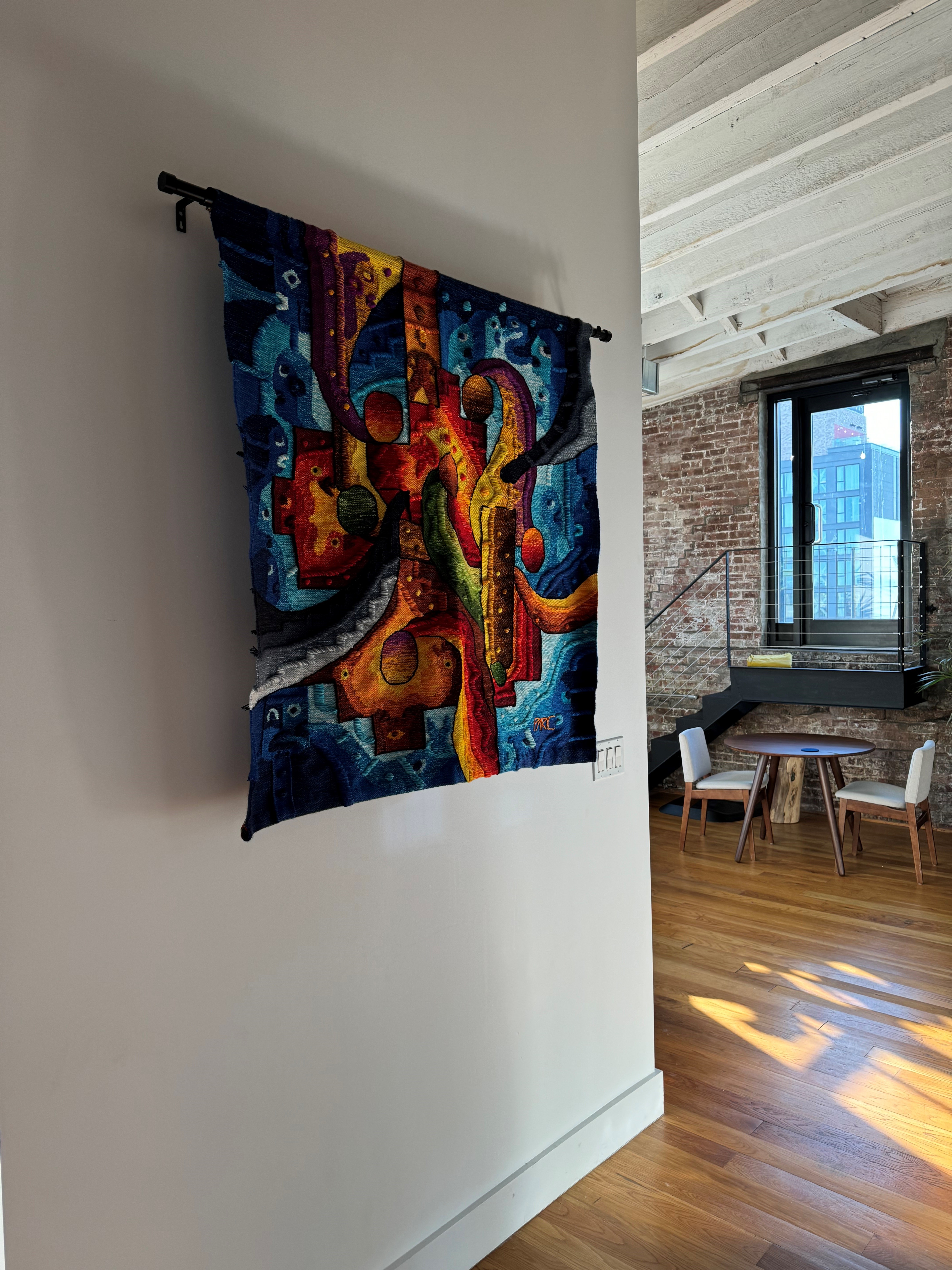 Colorful handwoven tapestry in a hallway looking toward the staircase and brick wall