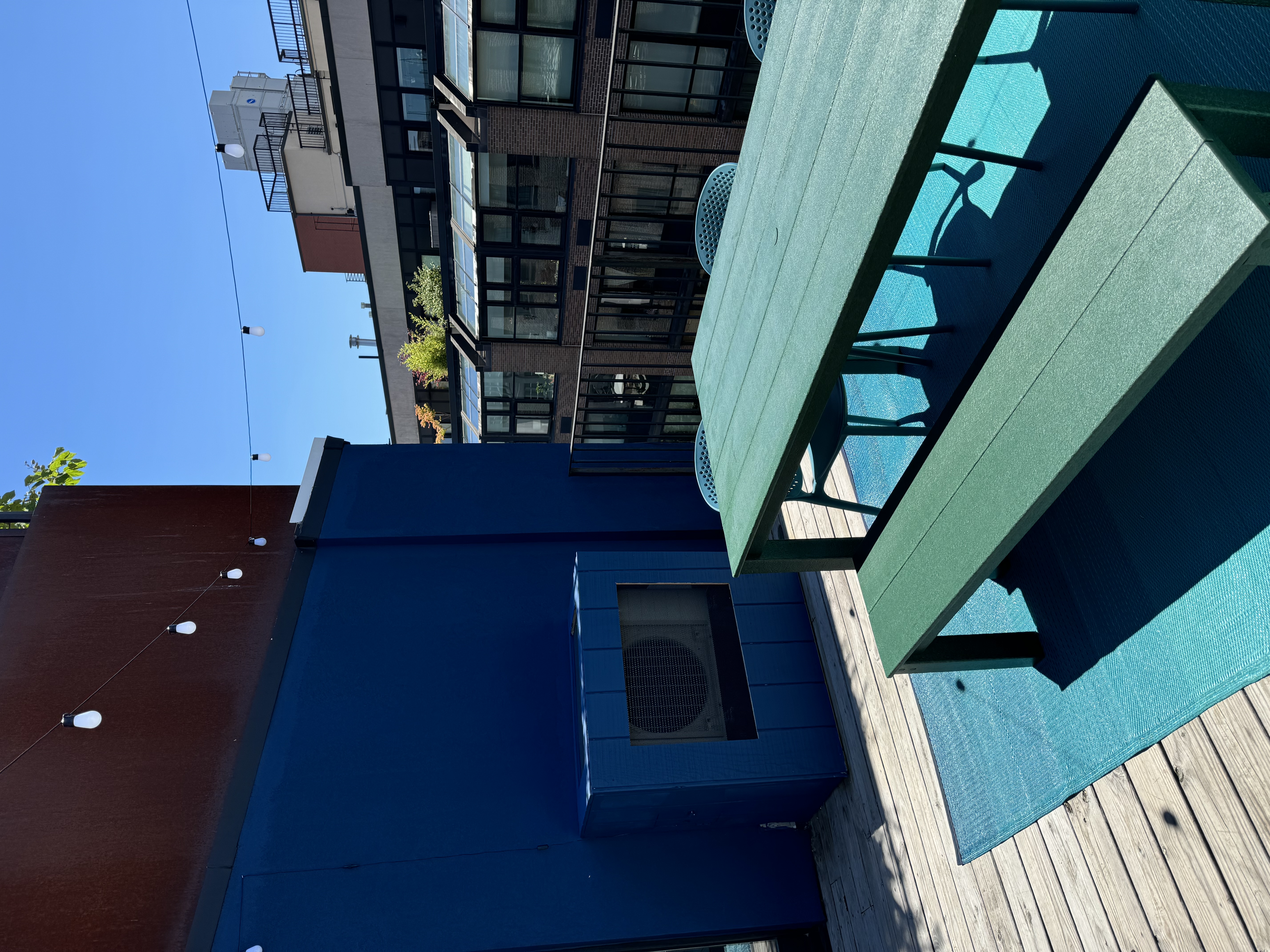 Sunny terrace deck with a green dining table and benches against a deep blue wall