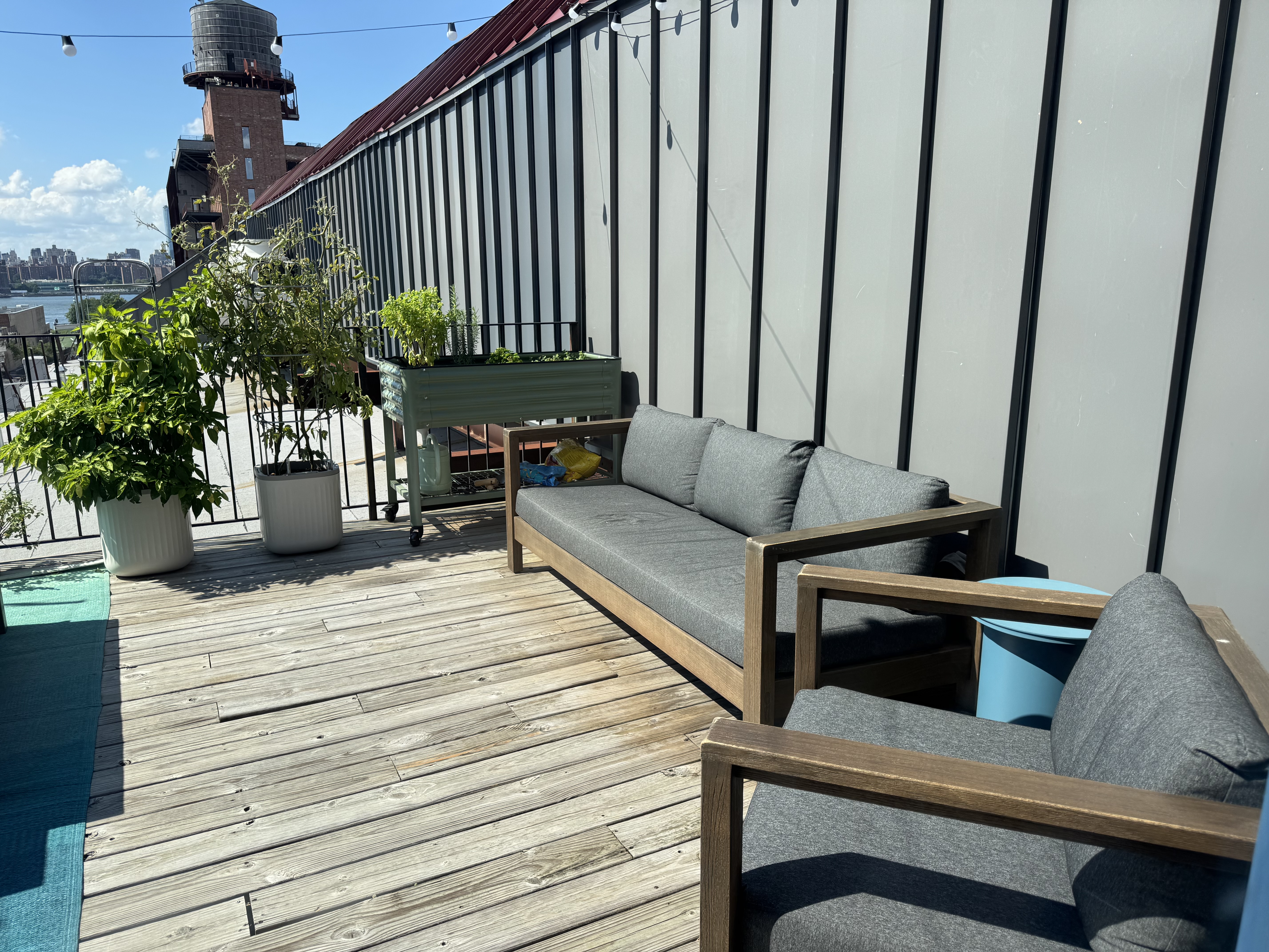Outdoor lounge corner of the terrace with a cushioned wood-frame couch and armchair beside the planters
